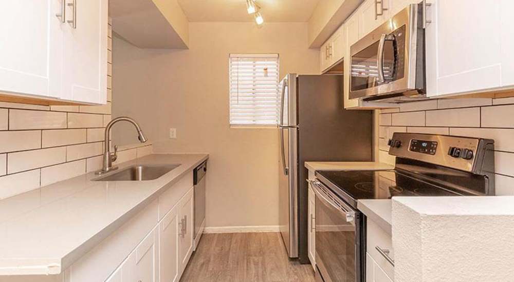 Modern kitchen with granite countertops, stainless steel appliances, and wood-style flooring at Fairways on Thunderbird in Phoenix, Arizona