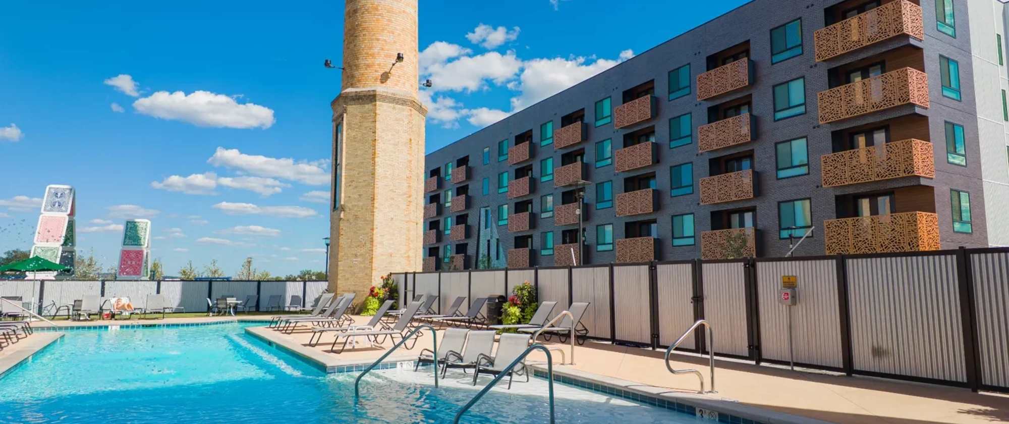 Resort-style outdoor pool at Factory 52 with lounge seating, skyline views, and the iconic historic smokestack.