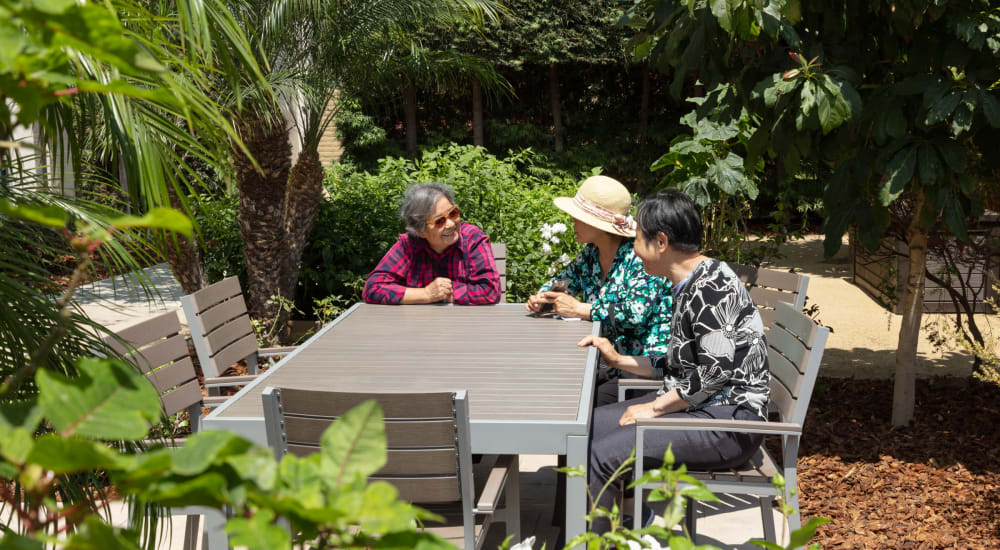 Residents chatting at a sunny patio table in the lush grounds at Golden West Tower Apts in Torrance, California