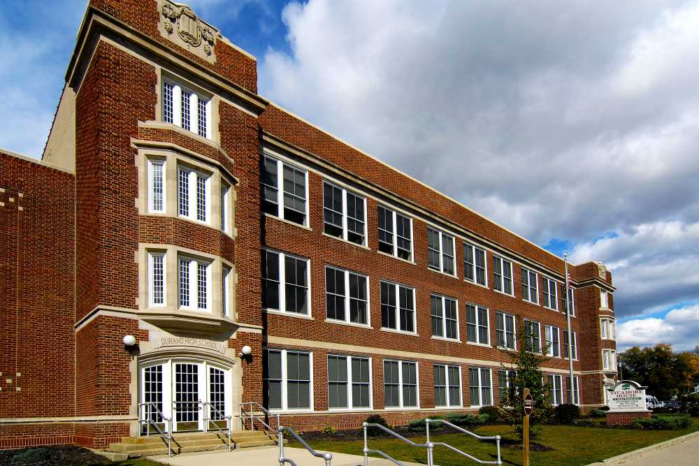 Historic brick apartment building with large windows and landscaped entrance at Sycamore House Senior Living in Durand, Michigan