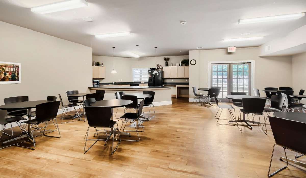 Community lounge with wood-style flooring, round tables, and kitchenette area featuring dark cabinetry at Lindbergh Parc Senior Apartments in Fort Worth, Texas