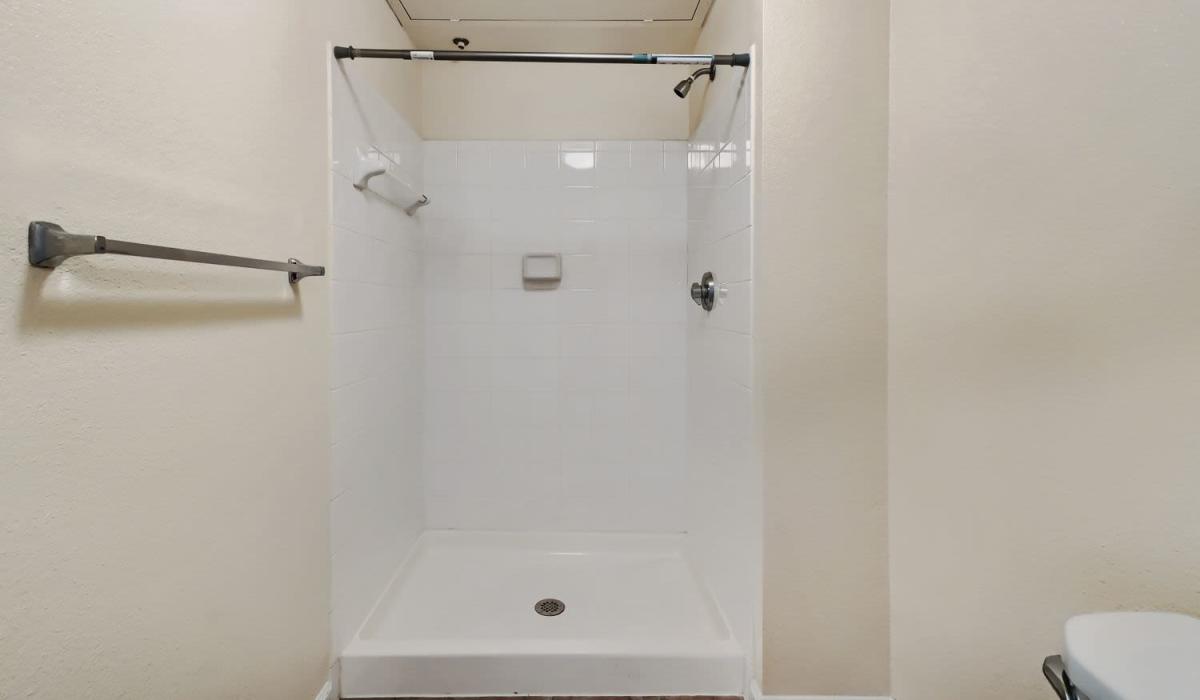 Clean, modern shower stall with white tiles and grab bars at Lindbergh Parc Senior Apartments in Fort Worth, Texas