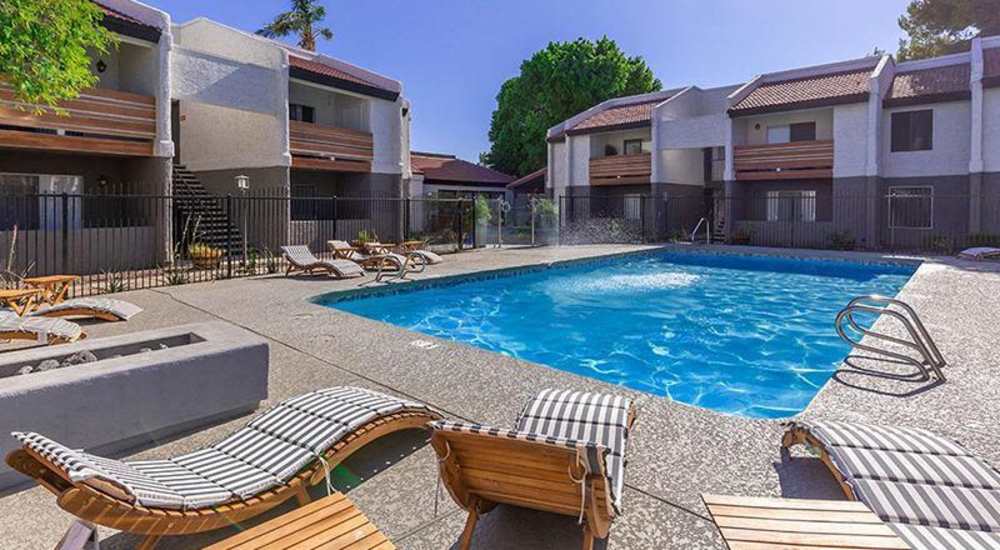 Resort-style pool surrounded by lounge chairs and landscaped courtyard with apartment buildings in the background at Fairways on Thunderbird in Phoenix, Arizona