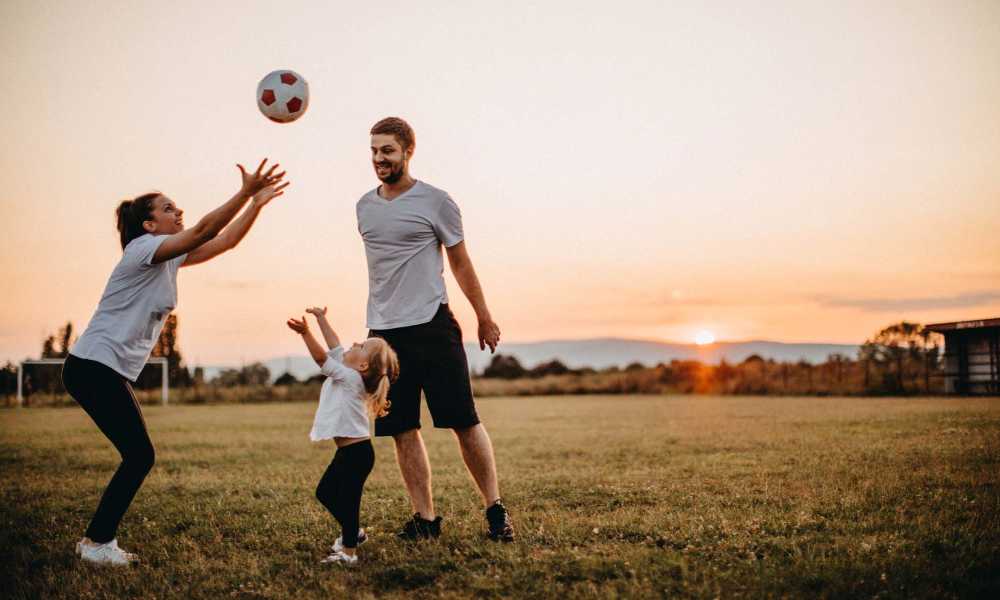 Family playing catch with a soccer ball in a grassy field at sunset at Everett at Port Wentworth in Port Wentworth, Georgia