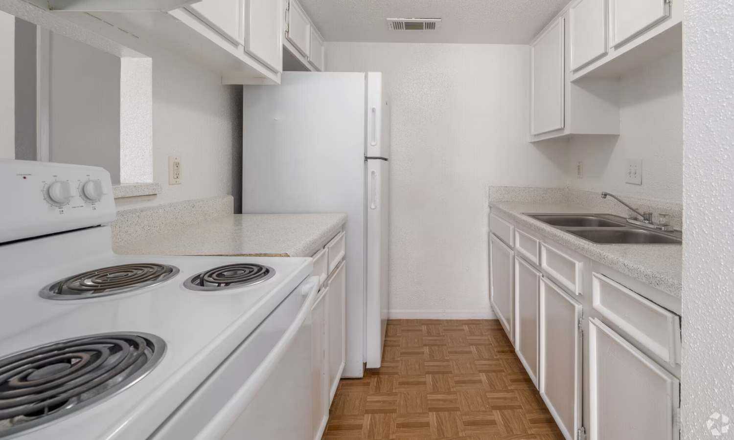 Galley kitchen with white appliances and cabinetry at Pecan Villa Apartments in Houston, Texas