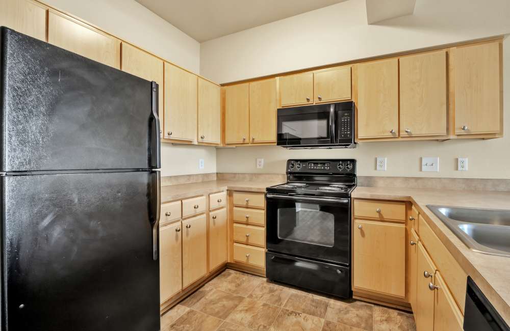 Cozy kitchen with wooden cabinetry and black appliances including microwave at North Main Village in Milwaukie, Oregon