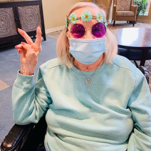 Resident in round purple glasses throwing up a 'peace' sign at The Oxford Grand Assisted Living & Memory Care in McKinney, Texas