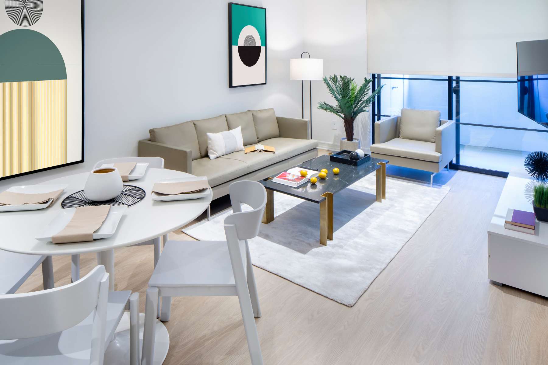 Modern living and dining area with beige seating, black coffee table, white dining set, and abstract wall art at Luxe Villas in Brentwood, California 
