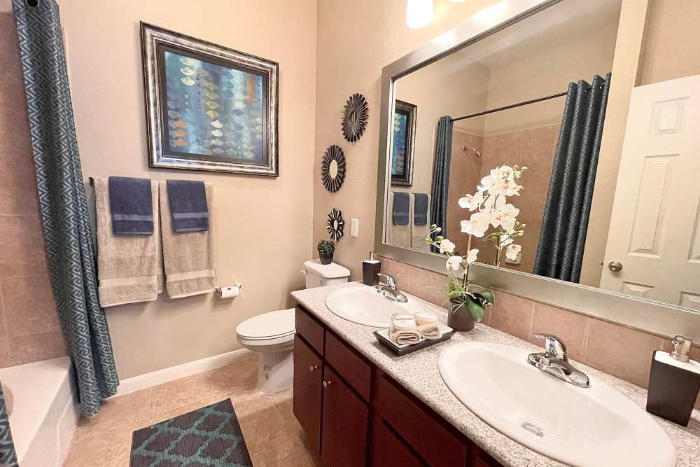 Modern bathroom with big mirror, sink, bath tub and wooden vanity at The Abbey at Stone Oak in San Antonio, Texas