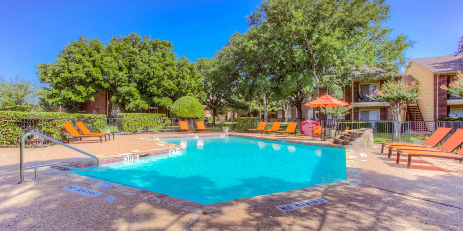 Charming poolside oasis with vibrant orange loungers and lush landscaping at Charter Oak in Euless, Texas.