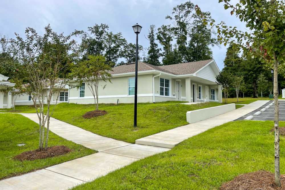 Gated entrance with landscaped pathways leading to modern apartment buildings and greenery at Village Springs Apartments in Defuniak Springs, Florida