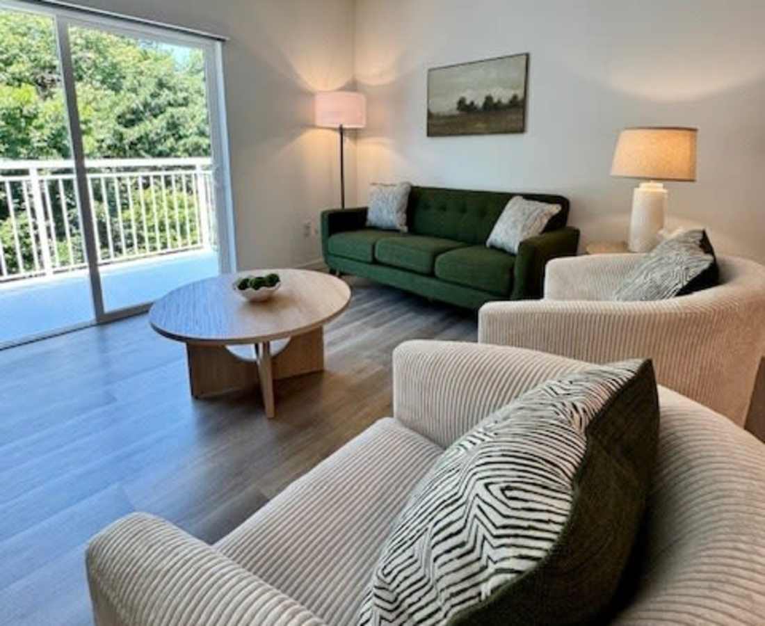 Green sofa with decorative pillows and lamp with natural lighting pouring in at Pritchard Park Place in Racine, Wisconsin