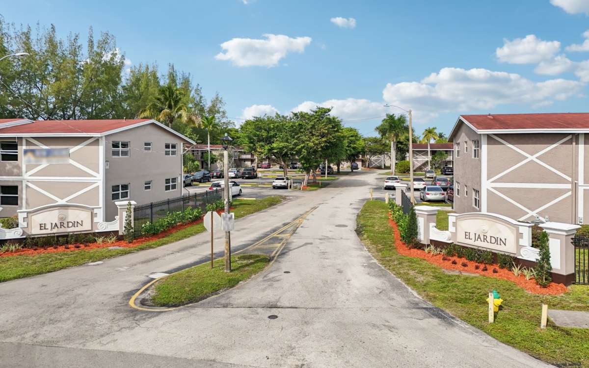 Entrance view of apartment buildings with property signage board at El Jardin Apartments in Hollywood, Florida