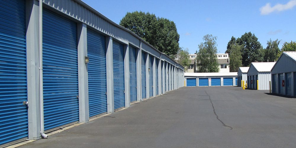 A wide, paved driveway along a row of storage units with blue doors at Van Mall Storage in Vancouver, Washington