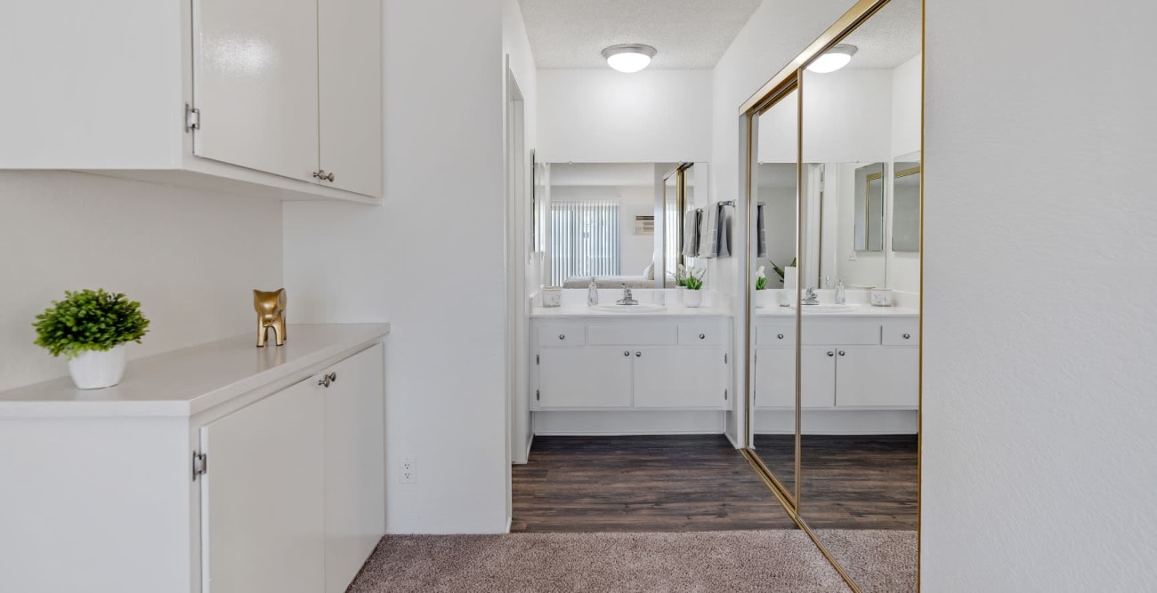 Walkway to the bathroom from bedroom, situated on the sides are wall cabinets and spacious closet with mirrored closet doors and a large vanity at The Windsor in Sherman Oaks, California