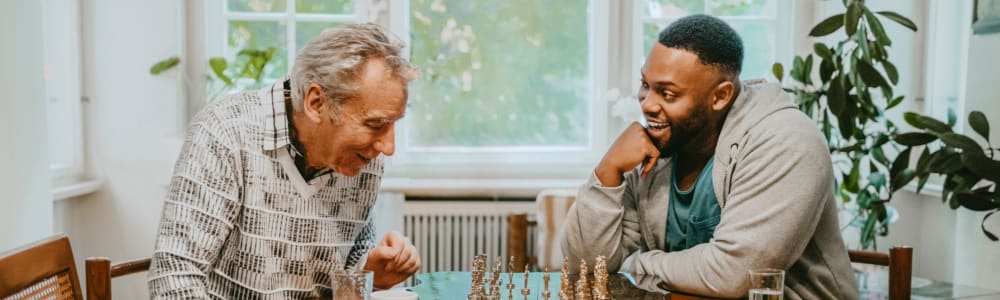 A resident playing chess in a common room with an employee