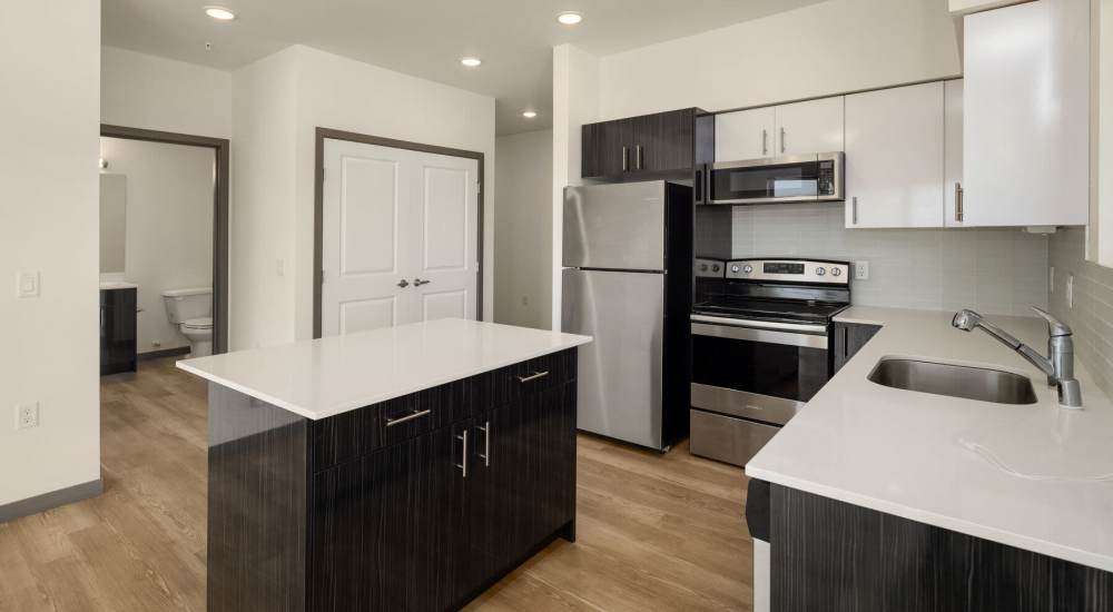 Open kitchen with sink, stove, microwave and wood flooring at Sixth & Alder Apartments in Tacoma, Washington