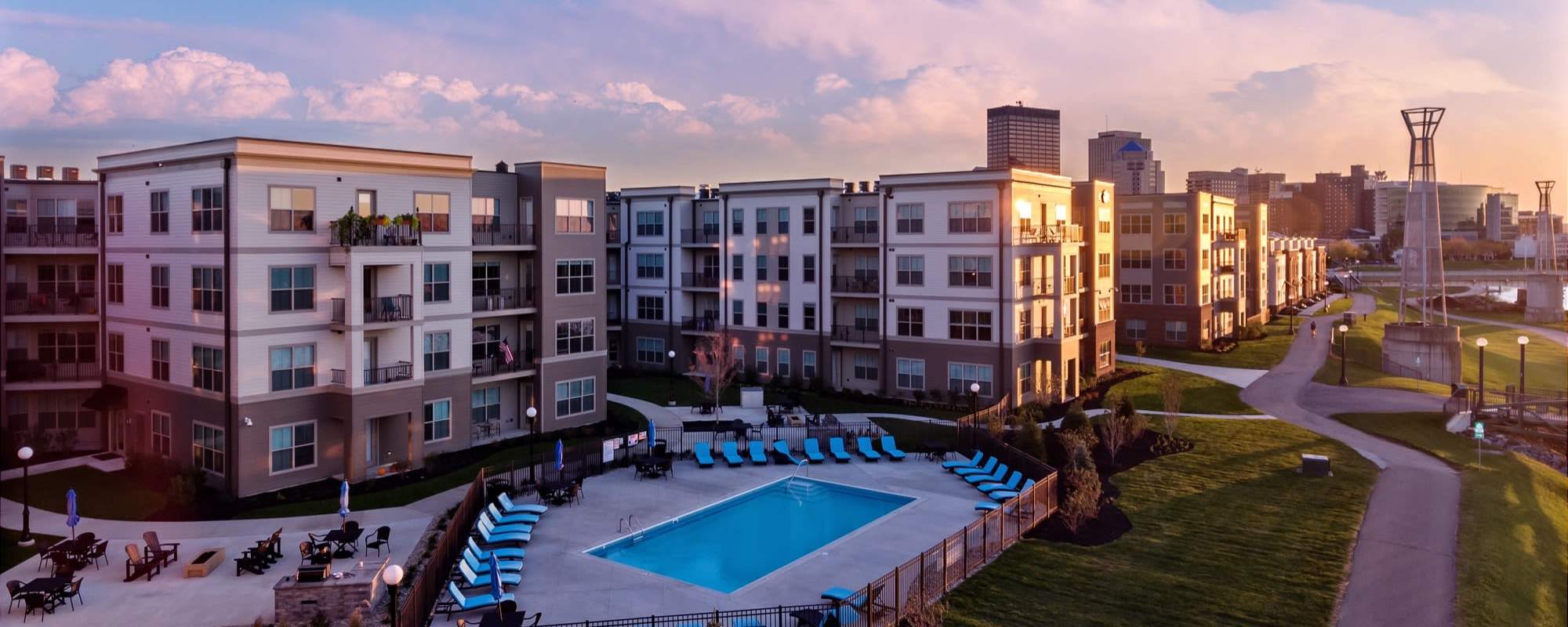 Resort-style pool surrounded by lounge chairs and landscaped grounds with walking paths at Water Street Apartments in Dayton, Ohio