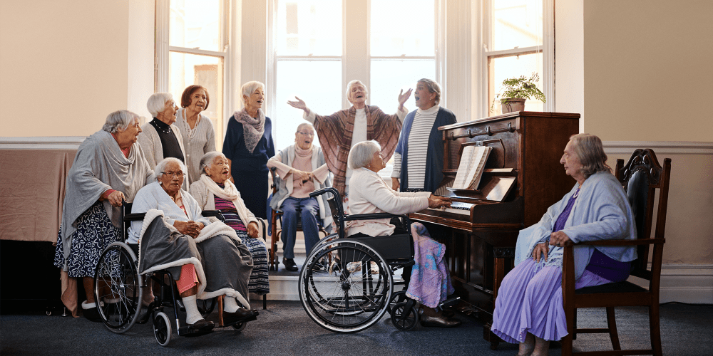 Standing and seated residents all singing together around a piano