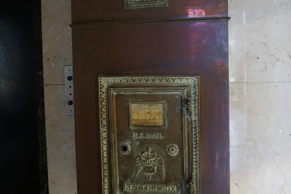 Vintage mail slot with ornate detailing in a marble lobby setting at 43 Town Square in Lima, Ohio