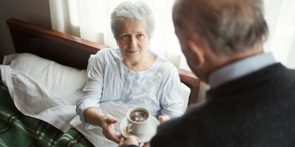 Resident in bed being served a cup of coffee at Fair Oaks Health Care Center in Crystal Lake, Illinois