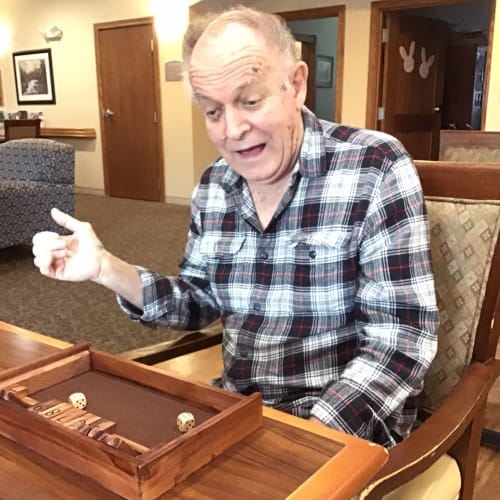 A resident playing a dice game at a wooden table inside Glen Carr House Memory Care in Derby, Kansas