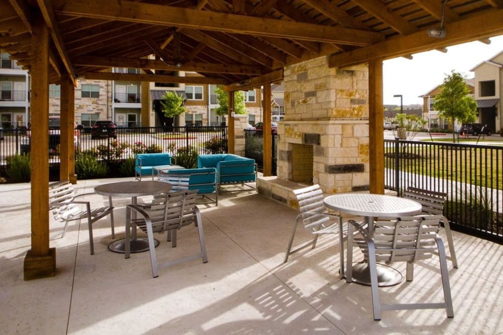 Covered outdoor lounge area with a stone fireplace at Biltmore at the Park in Pflugerville, Texas