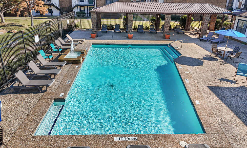 Resort style pool area with tanning chairs and pergola at Pine Oaks Apartments in Mesquite, Texas