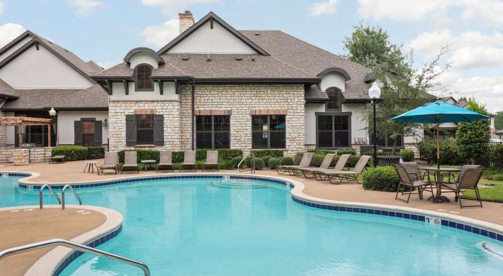 An apartment featuring a swimming pool with lounge chairs and tables at Stonebridge at the Ranch Apartments in Little Rock, Arkansas