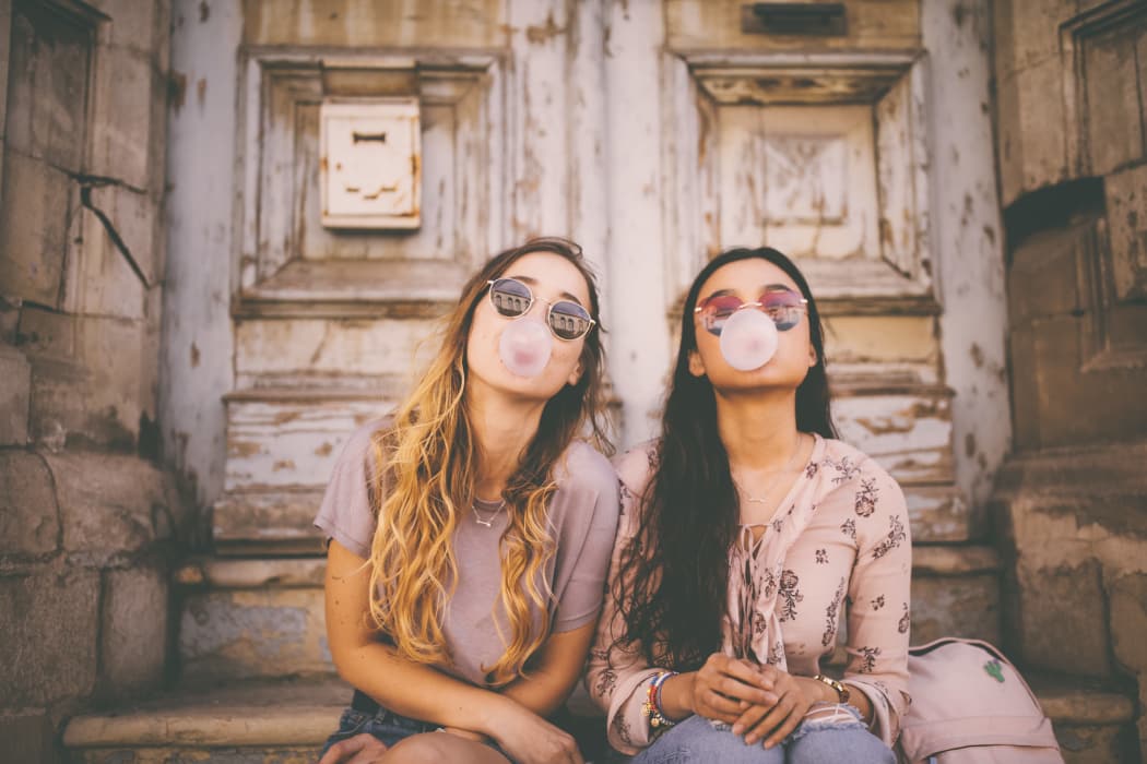 Teenage girls blowing bubbles with pink bubble gum in antique city streets near 23Hundred at Ridgeview in Plano, Texas