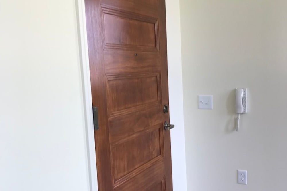 Wooden front door with a doorbell and light-colored walls in a welcoming entrance at Cavalier Greene in Corunna, Michigan