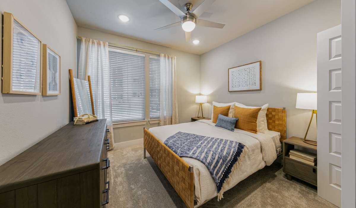 Well-lit apartment bedroom with ceiling fan, mirror and large window at The View at Belterra in Austin, Texas