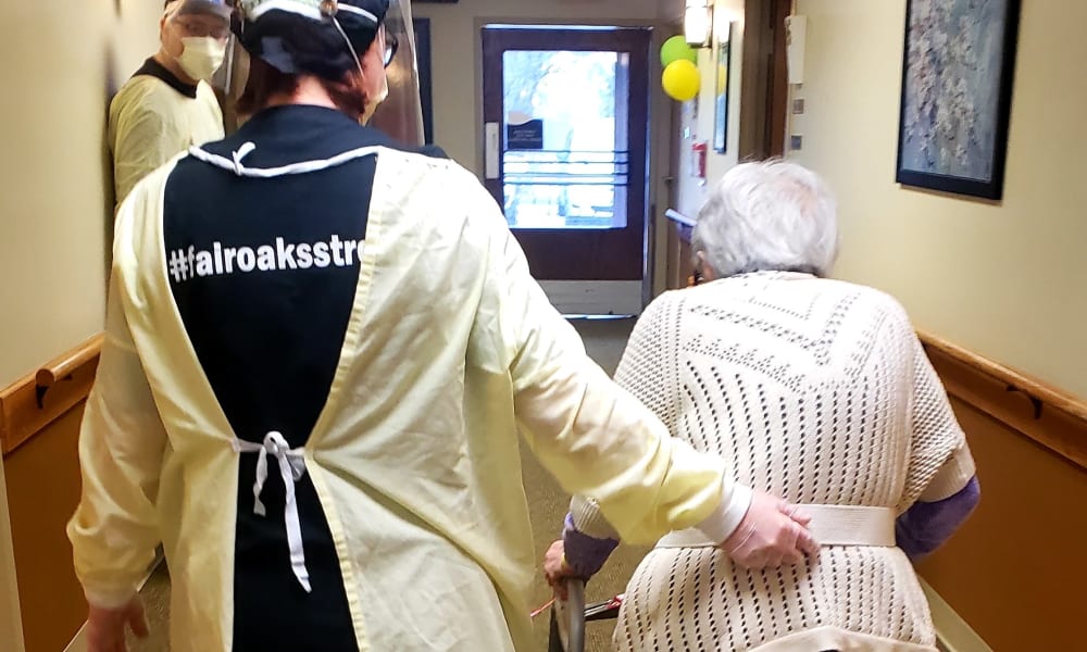 Caretaker in a medical gown walking with a resident at Fair Oaks Health Care Center in Crystal Lake, Illinois