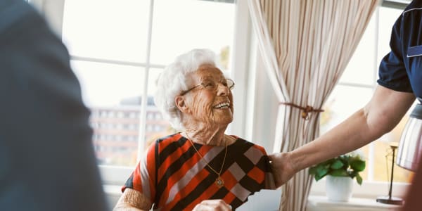 Resident sitting in a dining hall being greeted by a caretaker at a WISH community