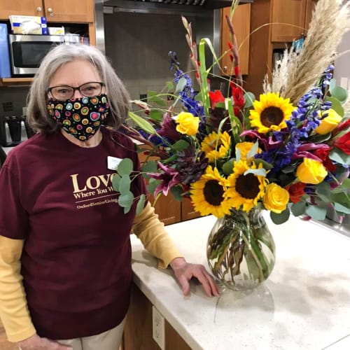 A resident standing next to a flower arrangement at Glen Carr House Memory Care in Derby, Kansas