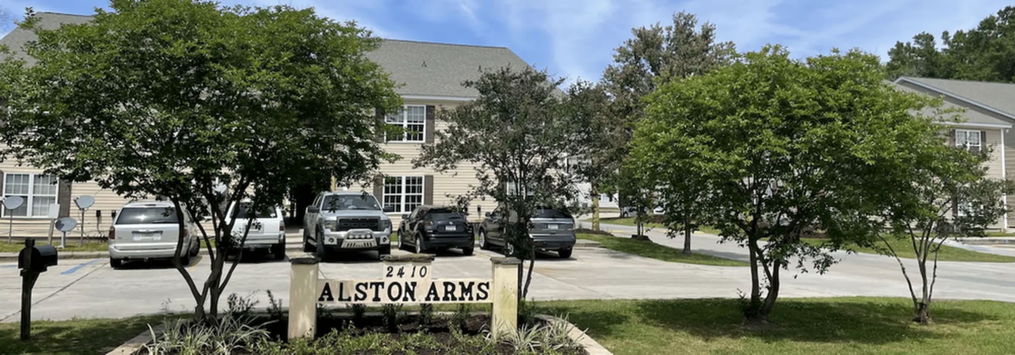 Exterior view of the community with parking and property signage at Alston Arms Apartments in North Charleston, South Carolina