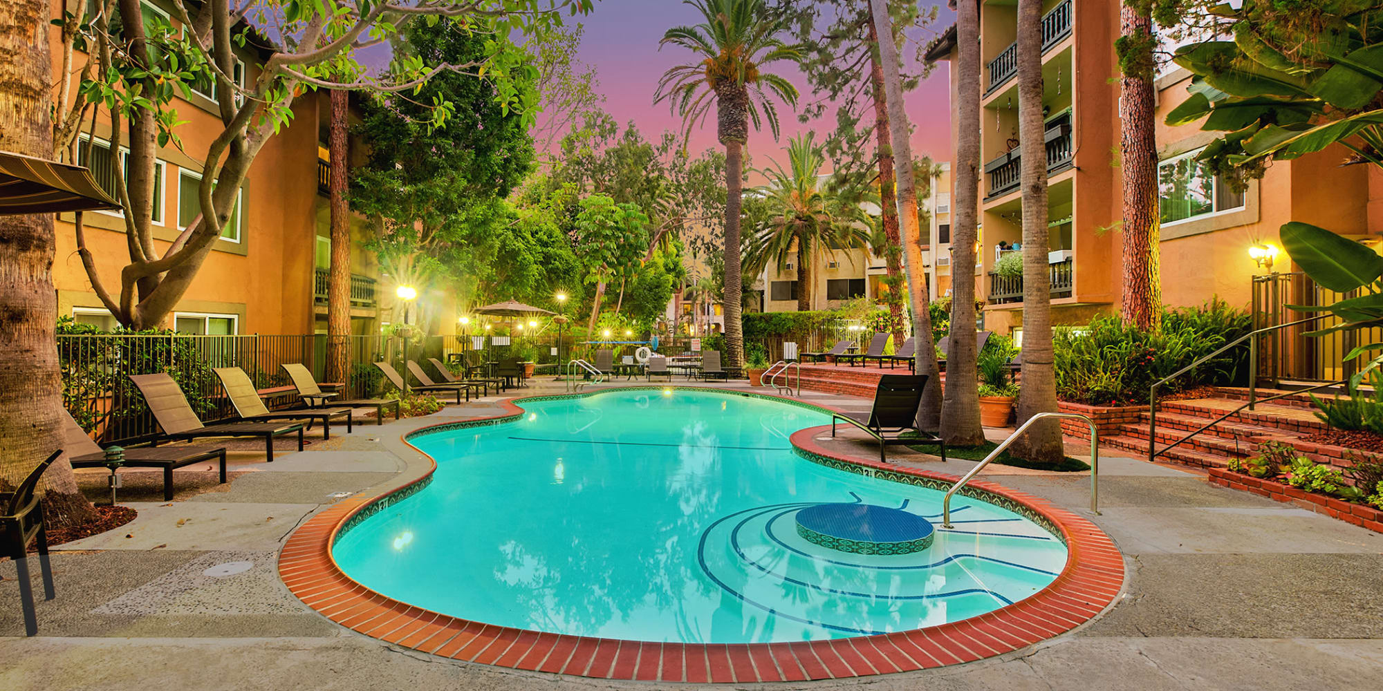 Early twilight at the swimming pool area surrounded by palm trees and lounge chairs at Casa Granada in Los Angeles, California