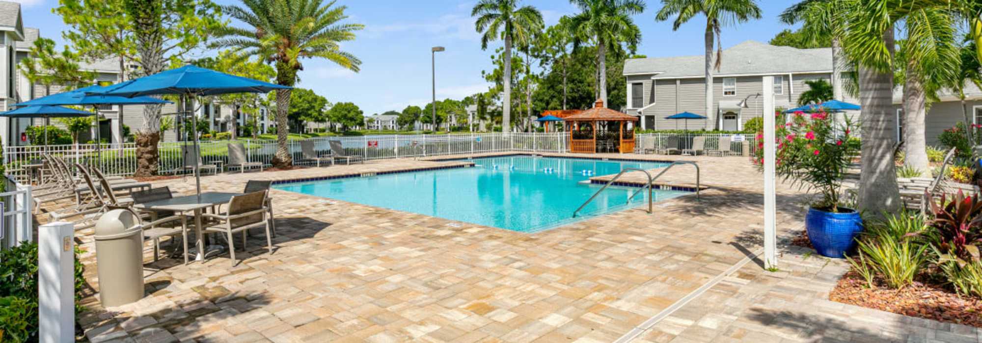 Swimming pool with sunshades and chairs at Woodmere Apartments of Venice in Venice, Florida