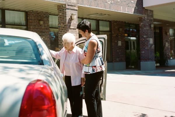 A staff member helping a resident into a car at Merrill Gardens. 