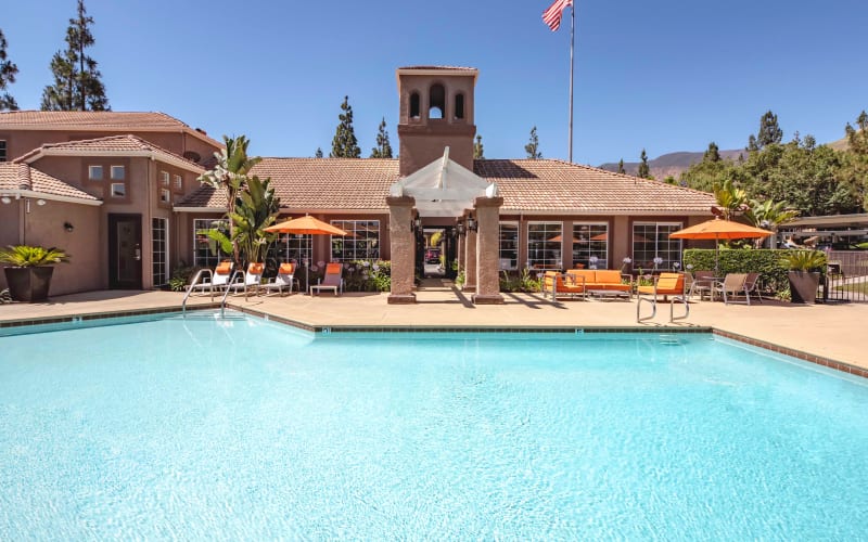 Large swimming pool with lounge chairs and umbrellas at Sierra Del Oro Apartments in Corona, California