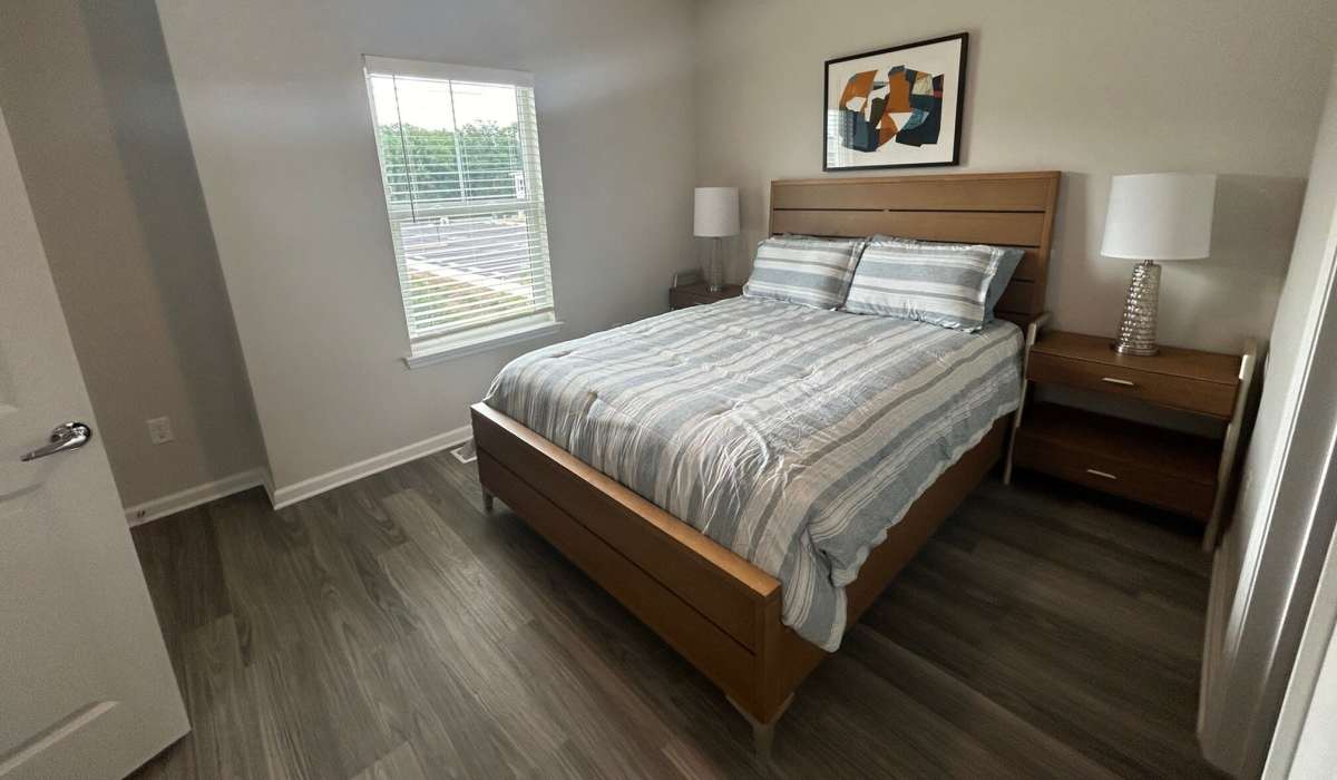 Comfortable bedroom with king size bed, side table lamp and wood-style flooring at Las Colinas in Foley, Alabama