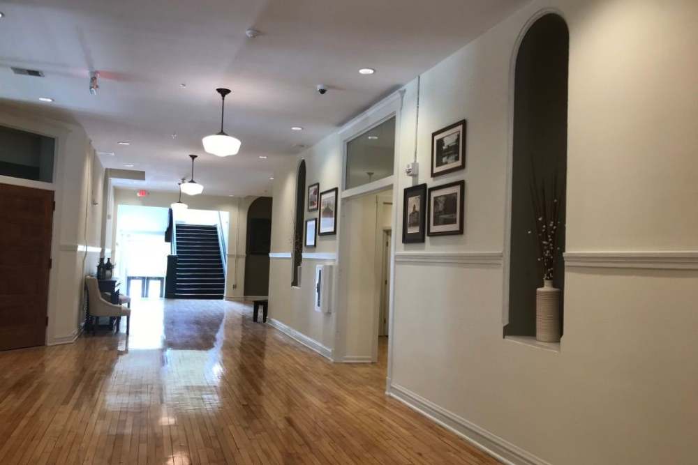 Welcoming hallway with hardwood flooring, decorative wall art, and natural light from large windows at Cavalier Greene in Corunna, Michigan