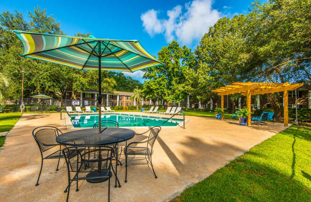 Sparkling pool surrounded by lush greenery and vibrant seating area at Avian Place Apartments in North Charleston, South Carolina