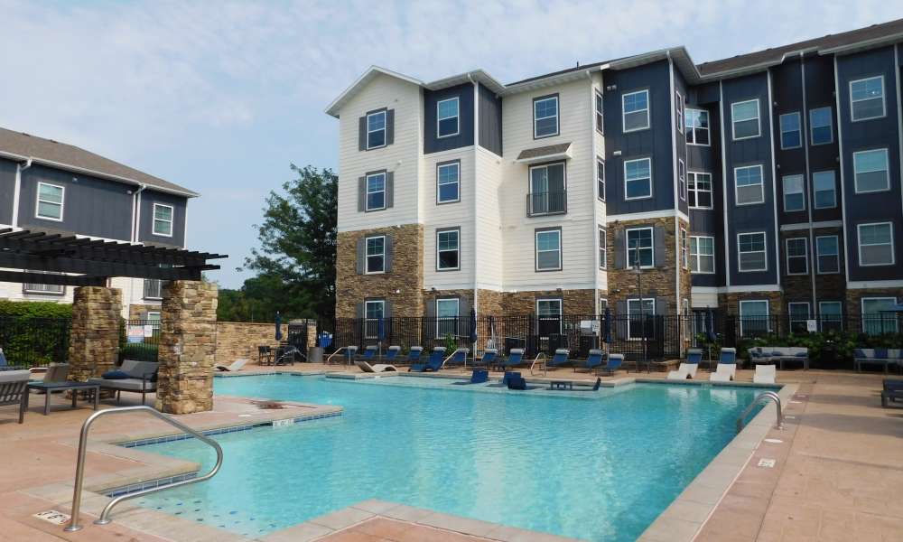 Outdoor swimming pool with lounge chairs beside a multi-story apartment building at The Den in Columbia, Missouri