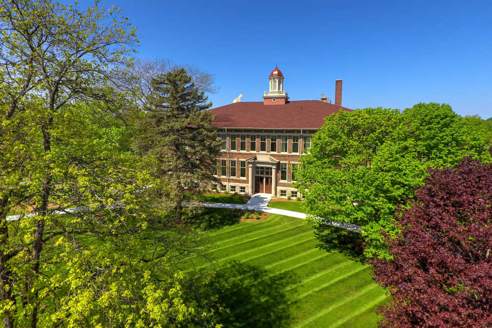 Historic building surrounded by lush greenery and manicured lawns with clear blue sky at Cavalier Greene in Corunna, Michigan