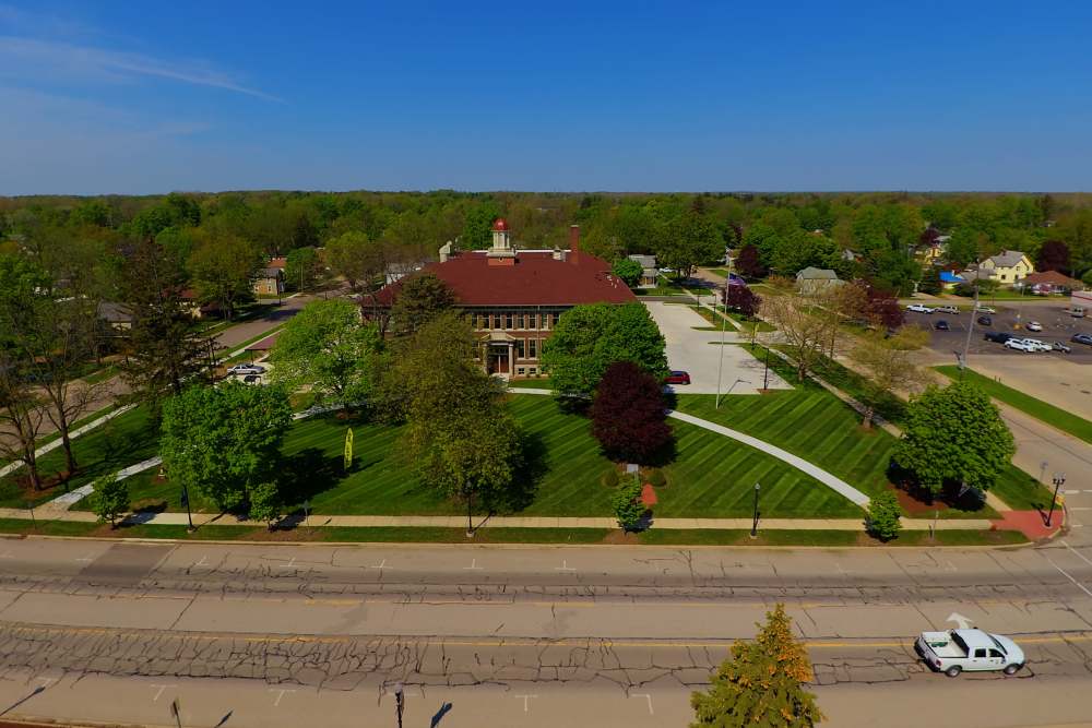 Scenic view of lush green landscaping surrounding a historic building and clear blue sky at Cavalier Greene in Corunna, Michigan
