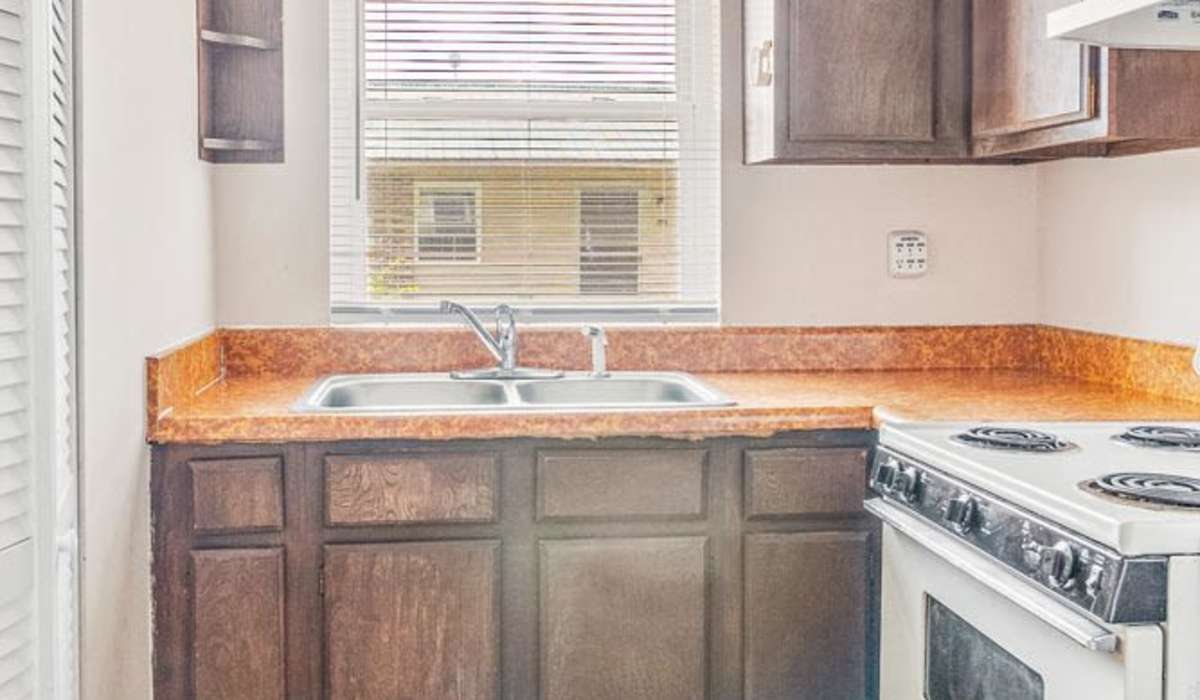 Kitchen with dark wood cabinets, double sink, and stove, featuring natural light from window at Walnut Street Apartments in Dickson, Tennessee