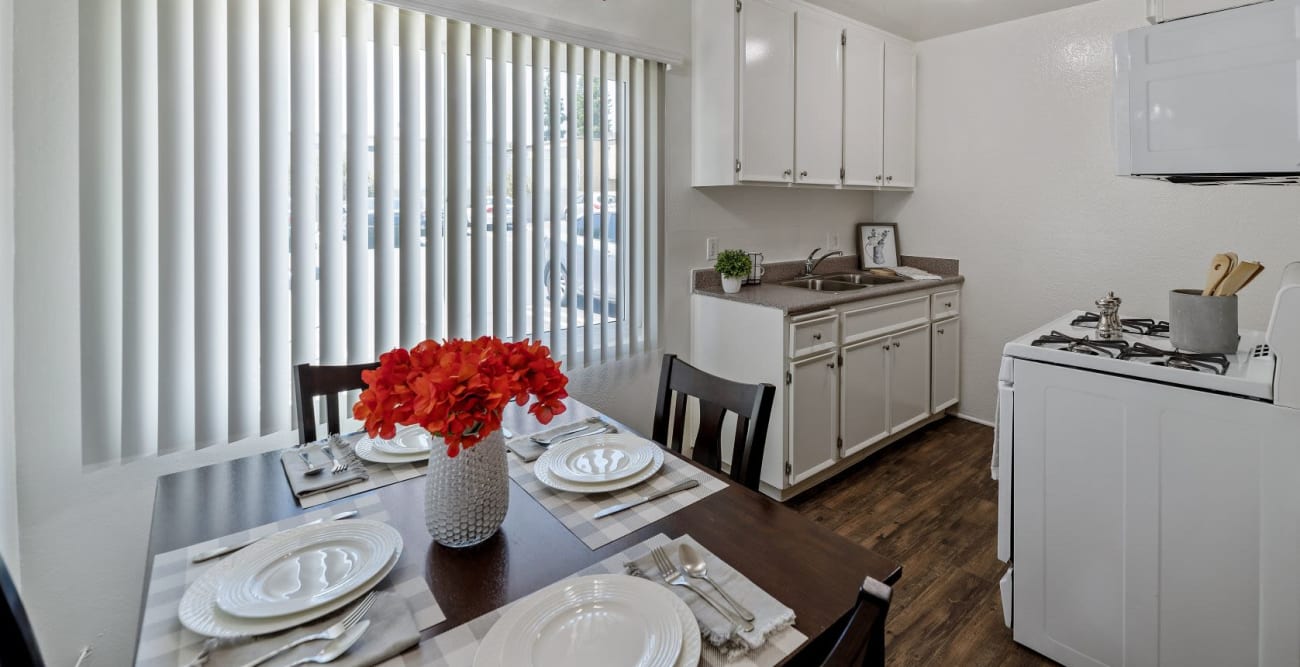 Open concept dining room and kitchen with plank flooring, gas range, and white kitchen cabinets for ample storage at The Windsor in Sherman Oaks, California