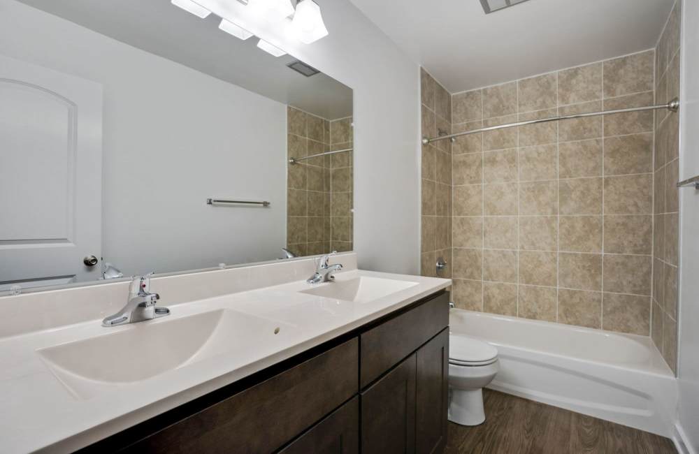 Modern bathroom with double sinks, tile backsplash, and wood-style flooring at Fairway Ridge in Baltimore, Maryland