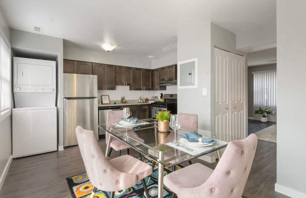 Modern kitchen with stainless steel appliances, granite counter tops, and dining area with glass table and pink chairs at Fairway Ridge in Baltimore, Maryland 